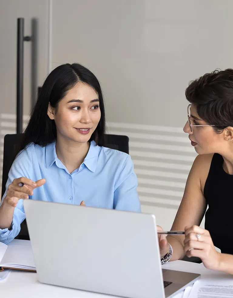 Two professional women engaged in a discussion in a modern office setting.